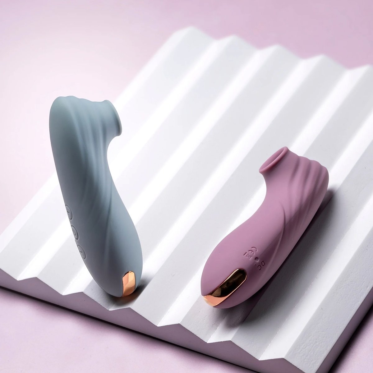Two clitoral suction stimulators in teal and pink colorways on a ridged white display